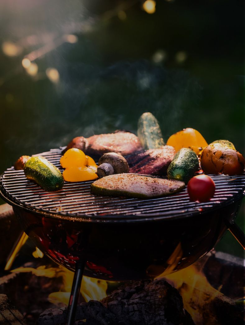バーベキューコンロの上で、お肉や野菜、キノコが炭火で美味しそうに焼かれている